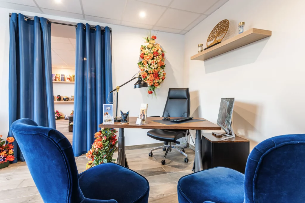 Bureau d'accueil des pompes funèbres avec fauteuils bleus et fleurs.