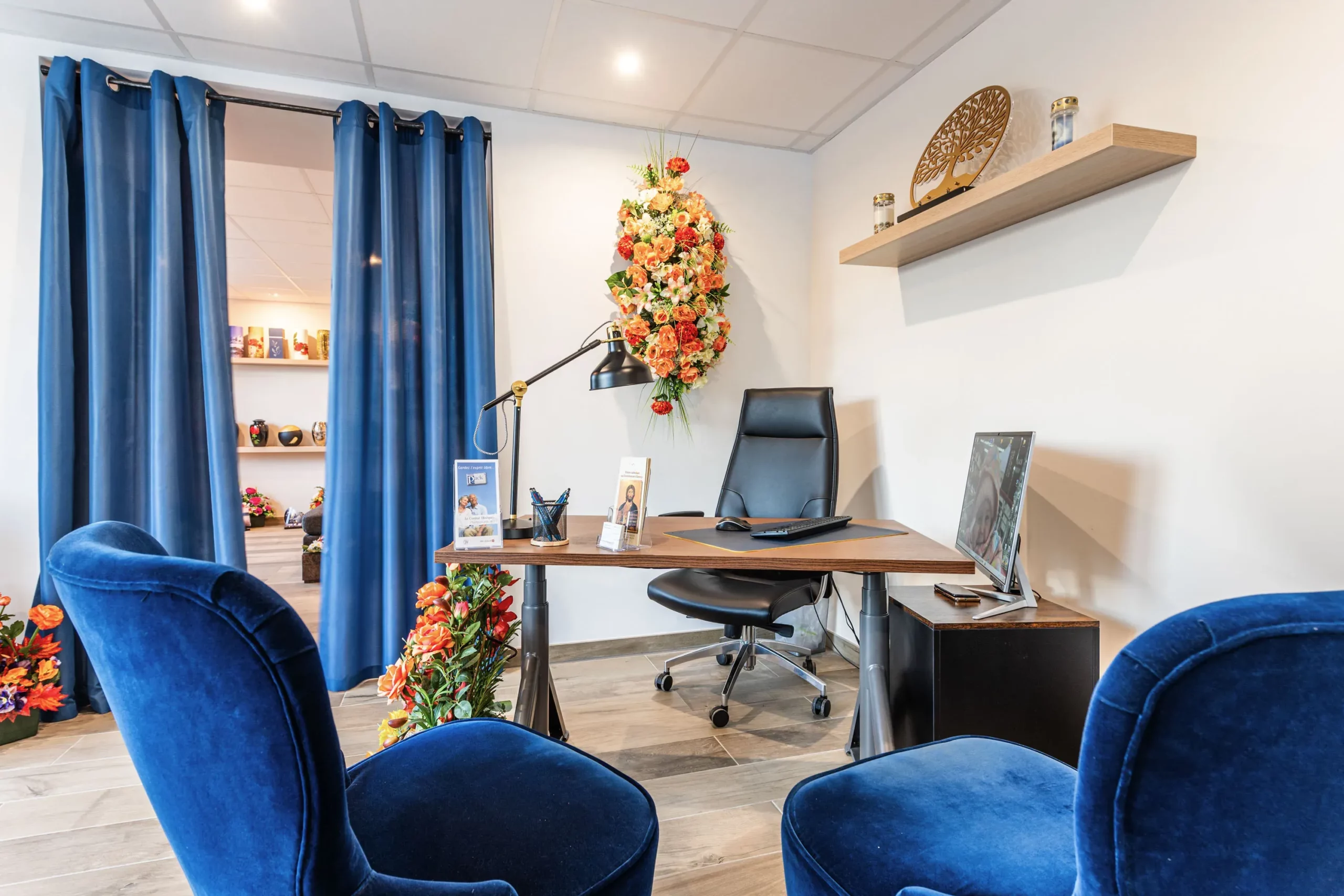 Bureau d'accueil des pompes funèbres avec fauteuils bleus et fleurs.