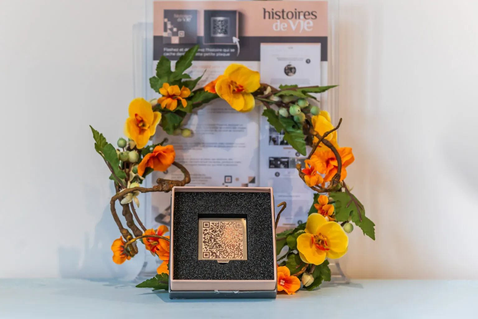 Présentation d'un code QR mémoriel dans un écrin, entouré de fleurs jaunes.