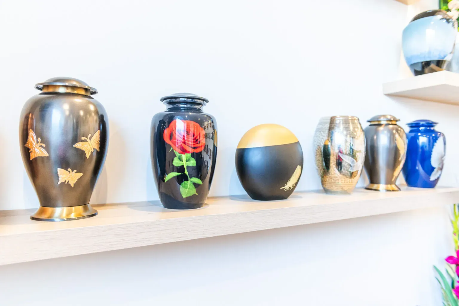 Différents modèles d'urnes funéraires décorées exposés sur une étagère en bois.